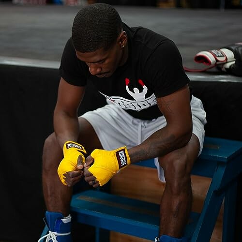 Boxer sitting on a bench with yellow hand wraps.