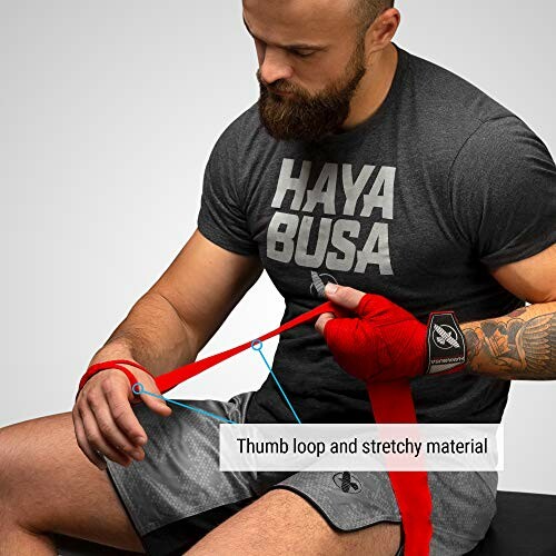 Man wearing Hayabusa shirt wrapping hands with red boxing wraps.